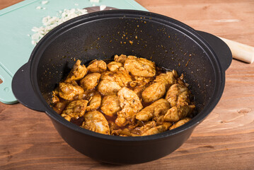 Cooking homemade chicken curry in a pan - fried chicken, and a board with chopped onions in the background