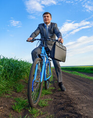 Businessman rides a bicycle in a green grass field - business concept for freedom, vacation or freelance. Beautiful spring nature.
