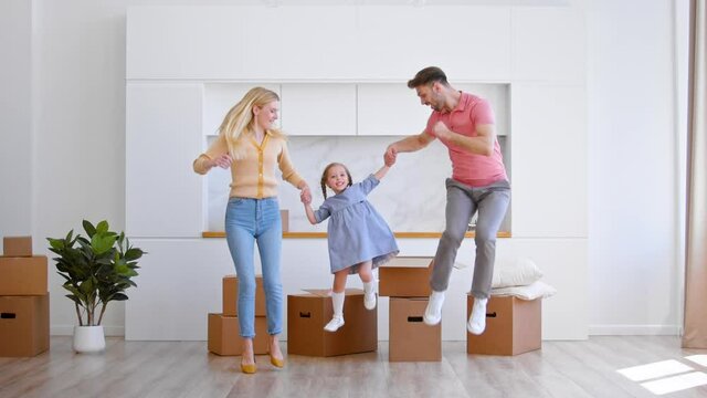 Amazed family jumps on brown wooden floor lifting daughter