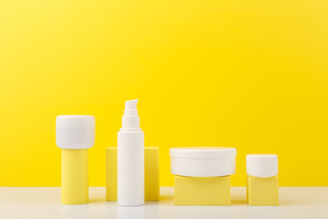Trendy colorful composition with set of cosmetic bottles with beauty products on geometric props against yellow background with copy space. Concept of creams with citrus extracts or skin products with