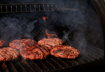 Homemade meat BBQ burgers patties for hamburger cooking on flaming grill barbecue with smoke.  Outdoor summertime meal. 