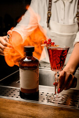 bottle and glass with cocktail decorated with caramel and berries are on bar