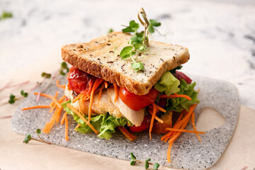 Board with tasty sandwich on light background, closeup
