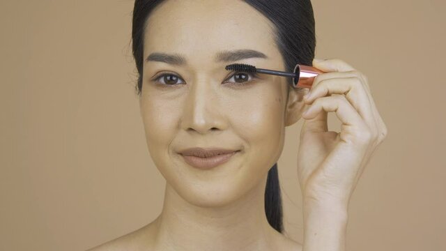 Beauty and Makeup concept, Portrait of Beautiful woman with perfect makeup at Studio. She using mascara to makeup her face.