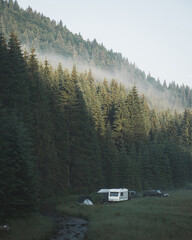 Beautiful view of a green mountainous landscape with trees and cars parked in a camping place