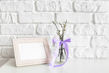 Willow branches with photo frame on table near brick wall