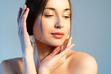 Fototapeta premium Facial skin care. Elegant woman. Spa beauty. Salon procedure. Peaceful gorgeous female with nude makeup touching smooth clean face isolated on blue.