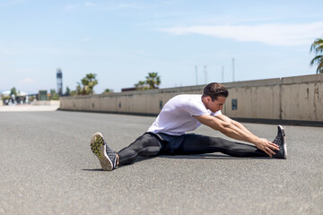 Fototapeta na wymiar Portrait of sitting runner outside doing stretch in street