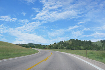 Scenic winding road along rolling hills and vegetation in Black Hills, South Dakota.
