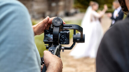 A cameraman recording a wedding ceremony using camera on a tripod - obrazy, fototapety, plakaty