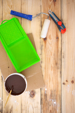a ditch, a clerical knife, paint and a roller on the surface of a wooden table are photographed from above