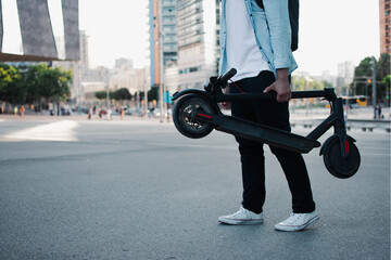 Fototapeta premium Young caucasian man transporting a electric scooter in the street.
