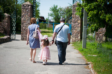 Fototapeta na wymiar family walking in the park. mom dad and little girl walking holding hands. back view. daughter in a pink dress. friendly loving family concept, love. outdoor, walk in the fresh air, threesome