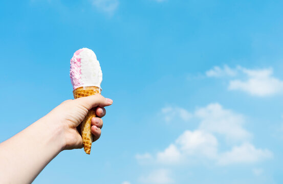 image of hand holding ice cream on blue sky background
