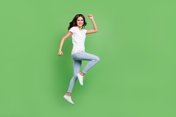 Fototapeta na wymiar Full size profile photo of cool brunette young lady jump hands fists wear t-shirt jeans isolated on green color background