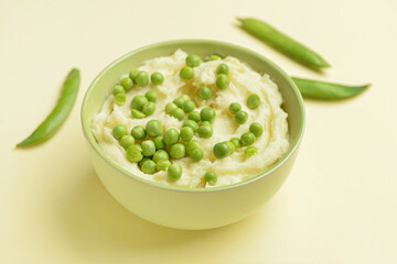 Bowl with mashed potatoes and green peas on color background