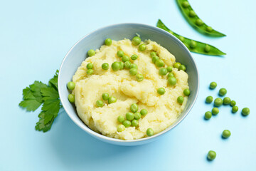 Bowl with mashed potatoes and green peas on color background