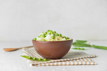 Bowl with mashed potatoes and green peas on light background