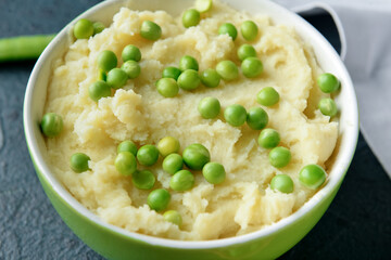 Bowl with mashed potatoes and green peas on color background, closeup