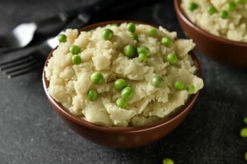 Bowl with mashed potatoes and green peas on dark background