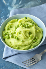 Bowl with mashed potatoes, green peas and fork on color background