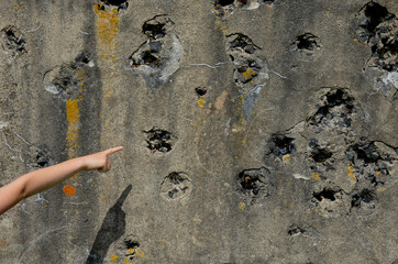 shot down concrete fortification with a machine gun. bullet holes pointed by the hand of a little boy. marveles at the terrible effect of the shooting