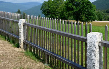 wooden fence made of natural planks. the columns are made of roughly worked gray granite. fencing land in the mountains. meadow trees sun. The planks are to the cut tip - Powered by Adobe