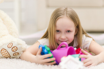 Cropped photo of blond girl laying on the floor with toys.
