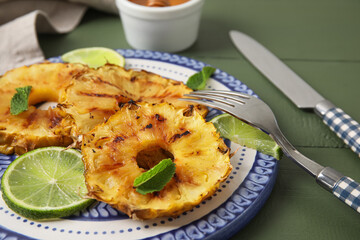 Plate with grilled pineapple slices and lime on color wooden background