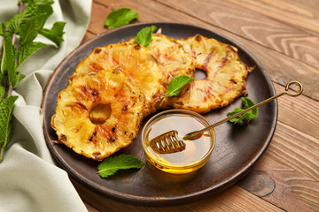 Plate with grilled pineapple slices and honey on wooden background