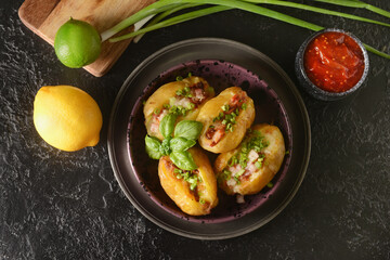 Plate with baked potato and sauce on dark background