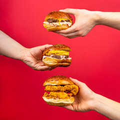 three human hands holding tasty hamburgers cheeseburger burger isolated on red background
