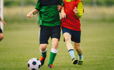 Two Soccer Players in a Duel on Grass Venue. Boys Running After Black and White Soccer Ball. Kids in Green and Red Soccer Jersey Kits and Cleats