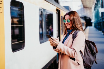 happy backpacker caucasian woman at platform on train station using mobile phone. Travel concept