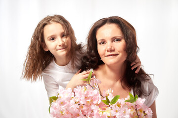 Daughter and mother with flowers in the studio on a white background. Teenager girl and woman posing indoors. Family during photo shoot in summer or spring time