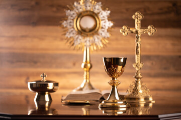 Fototapeta na wymiar Catholic religion concept. Catholic symbols composition. The Cross, monstrance, Holy Bible and golden chalice on brown background. 