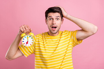Photo of amazed shocked young man hold hands alarm clock late palm head isolated on pink color...