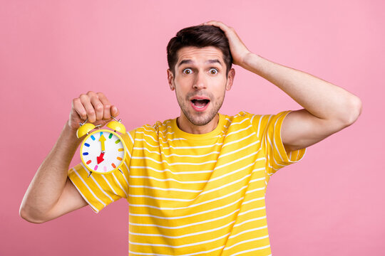 Photo of amazed shocked young man hold hands alarm clock late palm head isolated on pink color background