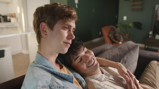 Young mixed race gay couple cuddling on the couch spending quality time together watching movie at home