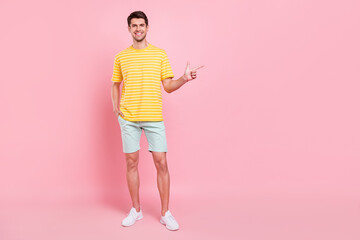 Full length body size view of attractive cheerful guy demonstrating copy space isolated over pink pastel color background