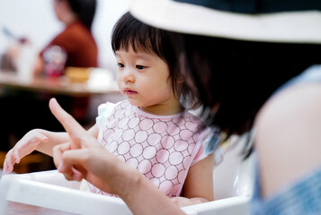 Asian baby girl listening acknowledge to her mother speaking about how to eat during launch time in restaurant.