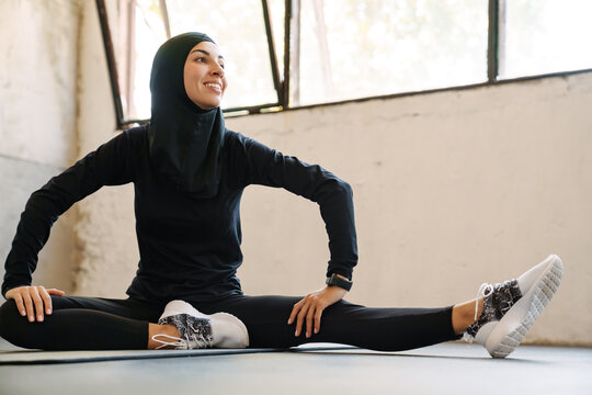 Young Muslim Sportswoman In Hijab Smiling While Working Out Indoors