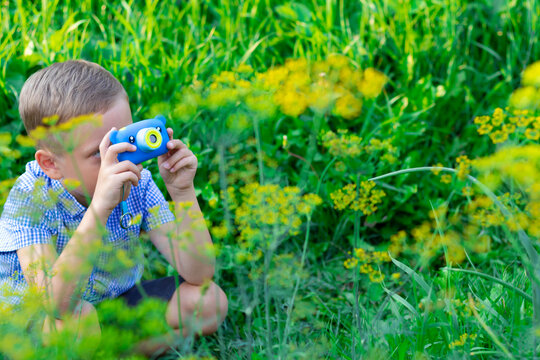 A cute preschool boy with a neat hairstyle in a blue shirt takes pictures of green plants on a hot summer day. Selective focus. Portrait