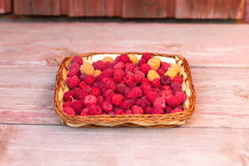 Fresh fragrant tasty red and yellow raspberries in a basket on a wooden background. Selective focus. Close-up