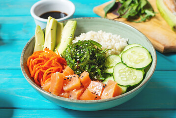 Salmon poke with avocado, seaweed, pickled carrots and cucumber on wooden table.