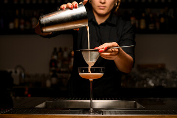 Woman bartender pours drink into glass by filtering it through sieve.