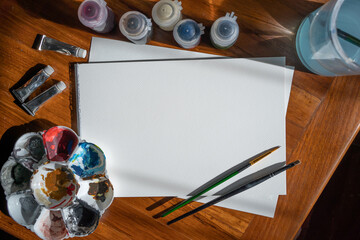 Paper, watercolor, acrylic color and painting equipment on wooden table