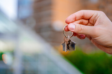 A man's hand holds the keys to a new house against the background of high-rise buildings