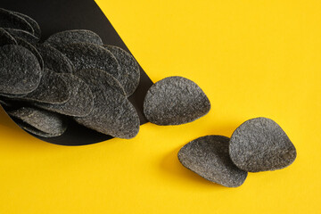 black potato chips in a black paper package on a yellow background, copy space