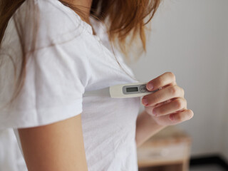 woman holding a thermometer under her arm behind a white t-shirt closeup